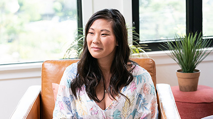 Allison, smiling in floral shirt, looking away. Plant on red table to the right.