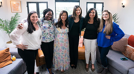 Smiling group of five women and a moderator, standing together.