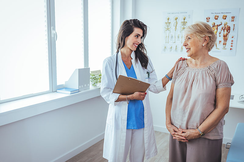 A female doctor with a clipboard talks to an older woman in a medical office