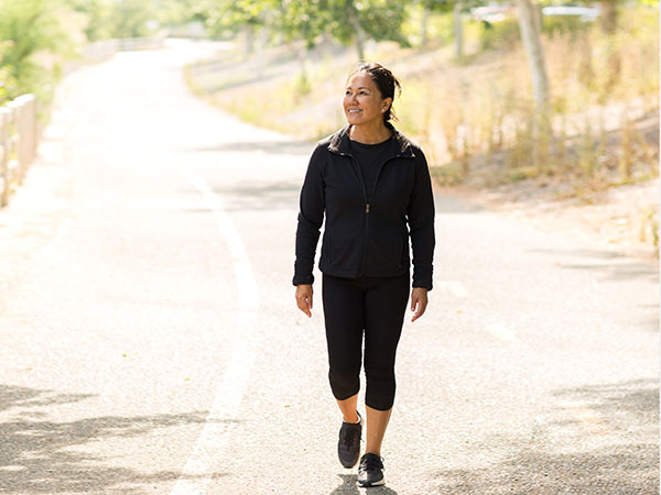 Person walking on a sunlit gravel path surrounded by trees.
