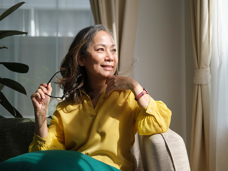 Woman in yellow blouse sitting on a couch, holding glasses and smiling.
