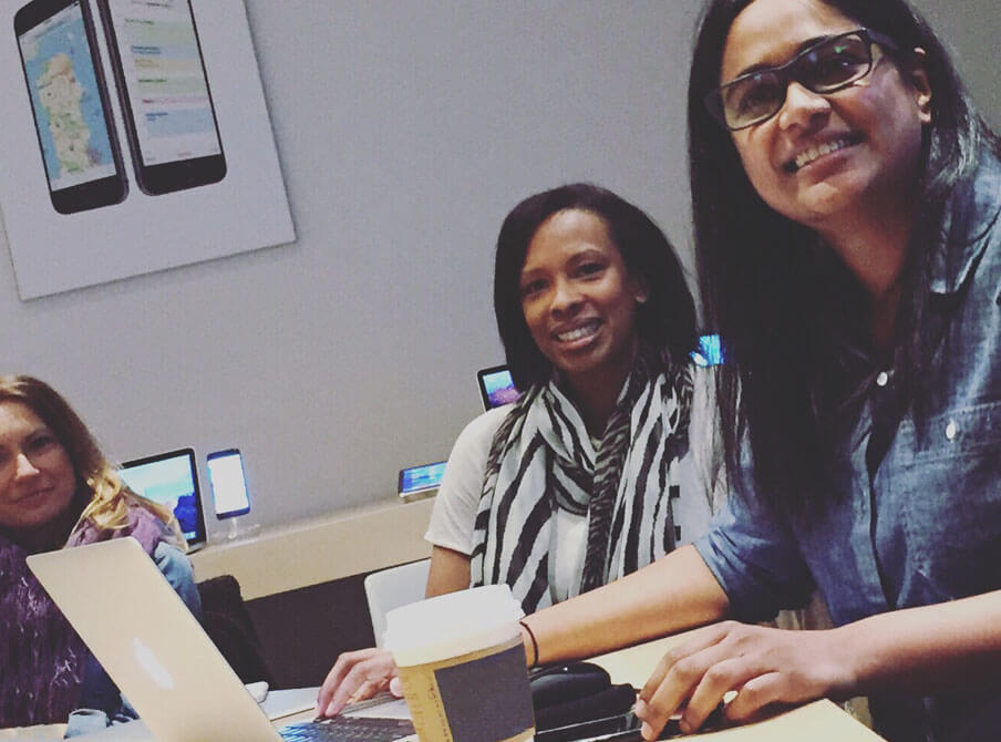 A group of people working on laptops in a modern space, with mobile devices displayed in the background and a coffee cup on the table.