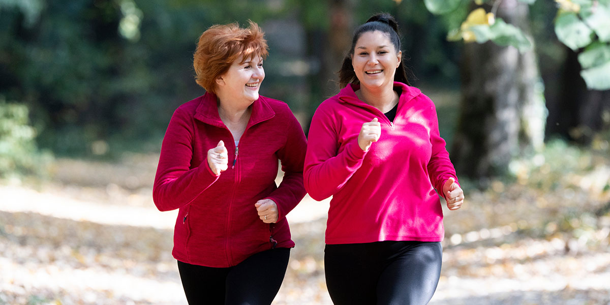 Dos mujeres trotan juntas en un parque, ambas sonriendo y vistiendo chaquetas rojas en combinación.