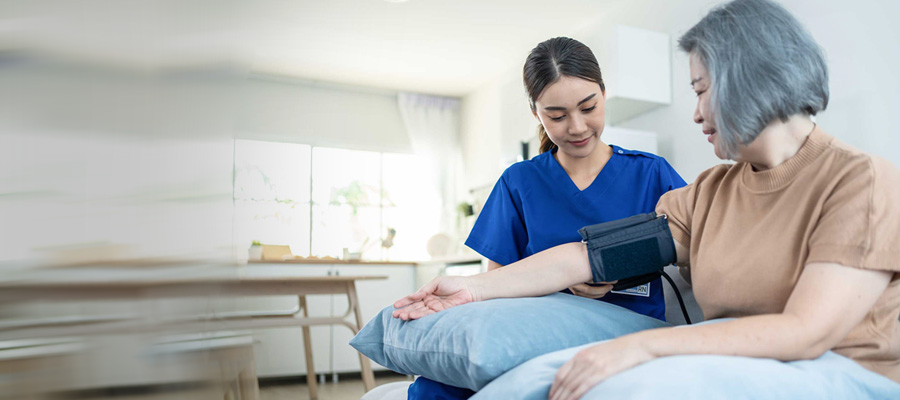 Healthcare worker measures an older woman’s blood pressure while her arm rests on a blue pillow.