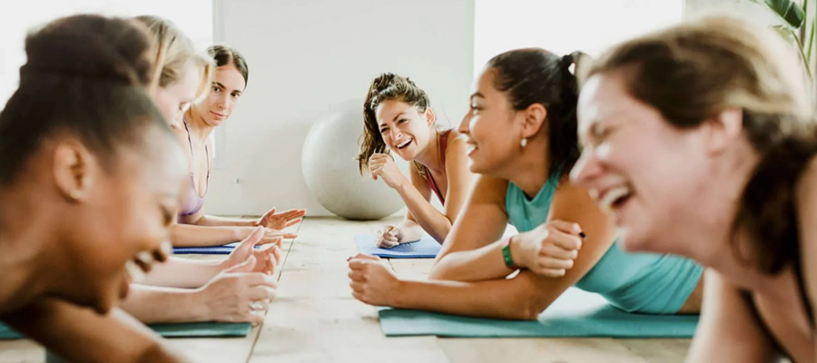 Group of adults laughing together during a floor-based exercise class on teal mats.