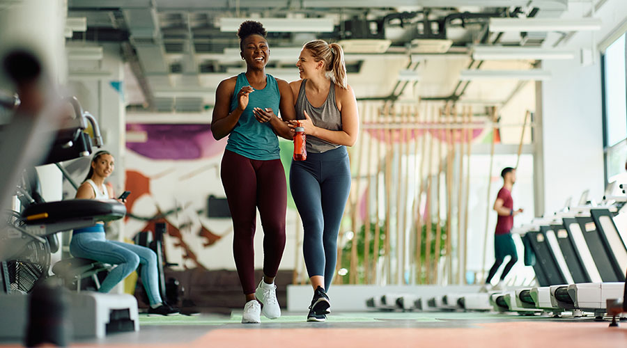 Two people walking and talking in a gym.