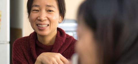 A person in a cozy maroon sweater gestures thoughtfully while engaging in conversation with another individual, seated nearby.