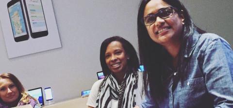A group of people working on laptops in a modern space, with mobile devices displayed in the background and a coffee cup on the table.