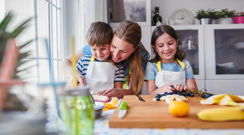 A mother and two children preparing food together in a kitchen.