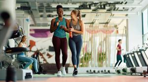 Dos personas caminando y hablando en un gimnasio.